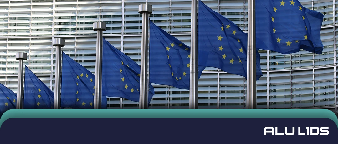 Flagi Unii Europejskiej przed szklanym budynkiem instytucji UE
